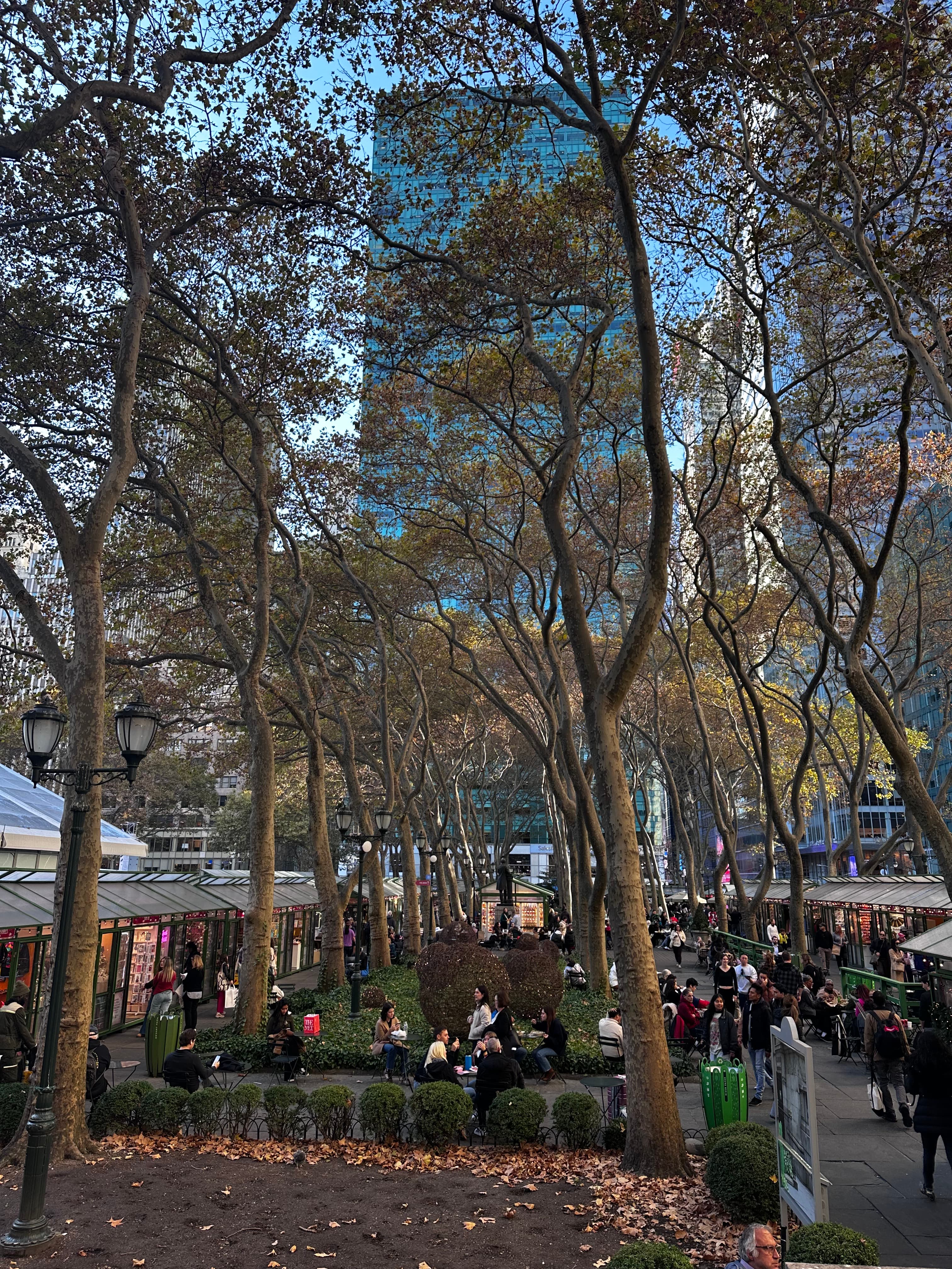 People walking and gathering beneath the trees in Bryant Park, New York